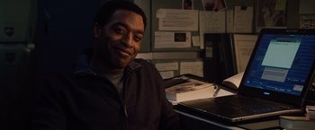 Movie still from “2012” (2009), directed by Roland Emmerich – A man sitting in front of a laptop computer; Medium shot, Over the shoulder angle