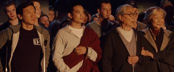 Movie still from “2012” (2009), directed by Roland Emmerich – A group of people standing in a room; Medium shot, Over the shoulder angle