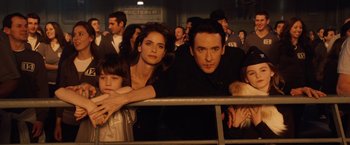 Movie still from “2012” (2009), directed by Roland Emmerich – A group of people sitting next to each other in front of a crowd; Close Up shot, Low angle