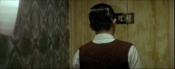 Movie still from “2046” (2004), directed by Kar-Wai Wong – A man in a brown vest is looking at a wall; Medium shot, Over the shoulder angle