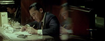Movie still from “2046” (2004), directed by Kar-Wai Wong – A man sitting at a table writing on a piece of paper; Medium shot, High angle