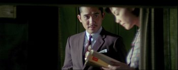 Movie still from “2046” (2004), directed by Kar-Wai Wong – A man wearing a suit and tie holding a book; Medium shot, Over the shoulder angle