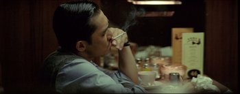 Movie still from “2046” (2004), directed by Kar-Wai Wong – A man sitting at a table with a cigarette in his mouth; Close Up shot, High angle