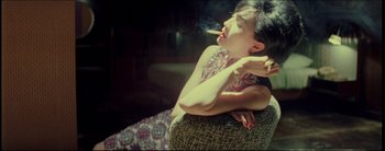 Movie still from “2046” (2004), directed by Kar-Wai Wong – A woman smoking a cigarette while sitting on a couch; Medium shot, High angle