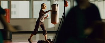 Movie still from “21” (2008), directed by Robert Luketic – A woman is boxing in a gym with a punching bag; Medium shot, Over the shoulder angle