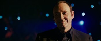 Movie still from “21” (2008), directed by Robert Luketic – A man in a black shirt and a black jacket smiling; Close Up shot, Over the shoulder angle