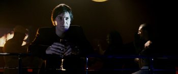 Movie still from “21” (2008), directed by Robert Luketic – A man holding a wine glass while sitting at a table; Medium shot, Over the shoulder angle