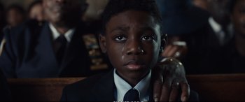 Movie still from “21 Bridges” (2019), directed by Brian Kirk – A boy in a suit and tie crying; Close Up shot, Over the shoulder angle