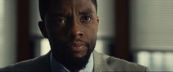 Movie still from “21 Bridges” (2019), directed by Brian Kirk – A person wearing a suit and tie; Close Up shot, Over the shoulder angle