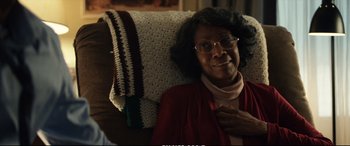 Movie still from “21 Bridges” (2019), directed by Brian Kirk – An older woman sitting in a chair with a crocheted blanket; Close Up shot, Over the shoulder angle