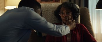 Movie still from “21 Bridges” (2019), directed by Brian Kirk – An older woman sitting on a couch with a man; Close Up shot, Over the shoulder angle