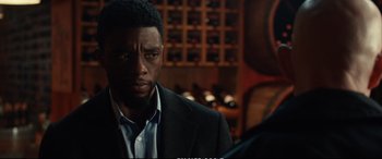 Movie still from “21 Bridges” (2019), directed by Brian Kirk – A man in a suit and tie in front of a wine cellar; Close Up shot, Over the shoulder angle