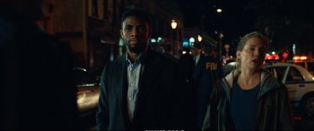 Movie still from “21 Bridges” (2019), directed by Brian Kirk – A man standing in the street at night; Medium shot, Low angle