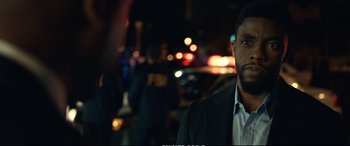 Movie still from “21 Bridges” (2019), directed by Brian Kirk – A man standing in front of a car at night; Close Up shot, Over the shoulder angle
