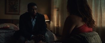 Movie still from “21 Bridges” (2019), directed by Brian Kirk – A man and a woman sitting on a couch in front of a window; Medium shot, Over the shoulder angle