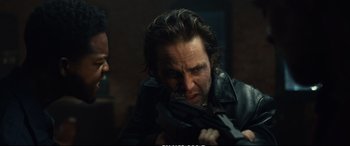 Movie still from “21 Bridges” (2019), directed by Brian Kirk – A man holding a gun while another man looks on; Close Up shot, Over the shoulder angle