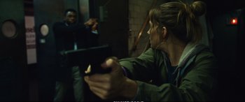 Movie still from “21 Bridges” (2019), directed by Brian Kirk – A woman holding a remote control in her hand; Medium shot, Over the shoulder angle