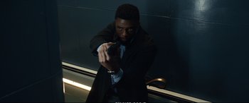 Movie still from “21 Bridges” (2019), directed by Brian Kirk – A man in a suit and tie holding a gun in his hand; Medium shot, Low angle