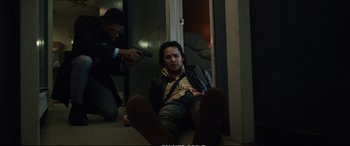 Movie still from “21 Bridges” (2019), directed by Brian Kirk – A man is sitting on the ground while another man holds a gun in his hand; Medium shot, Low angle