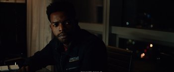 Movie still from “21 Bridges” (2019), directed by Brian Kirk – A man sitting on top of a wooden bench in the dark; Close Up shot, Over the shoulder angle