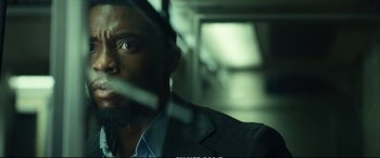 Movie still from “21 Bridges” (2019), directed by Brian Kirk – A man in a gray suit is looking out a window; Close Up shot, Low angle
