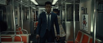 Movie still from “21 Bridges” (2019), directed by Brian Kirk – A man wearing a suit and tie standing on a train; Medium shot, Low angle