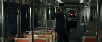 Movie still from “21 Bridges” (2019), directed by Brian Kirk – A man in a suit and tie holding a gun in a subway car; Medium shot, Over the shoulder angle