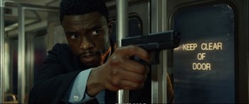 Movie still from “21 Bridges” (2019), directed by Brian Kirk – A man holding a gun while standing on a train; Close Up shot, Low angle