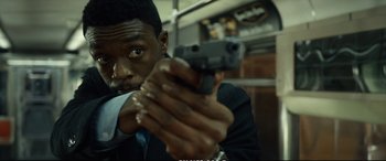 Movie still from “21 Bridges” (2019), directed by Brian Kirk – A man holding a gun while standing on a train; Close Up shot, Over the shoulder angle