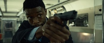 Movie still from “21 Bridges” (2019), directed by Brian Kirk – A man holding a gun while sitting on a train; Close Up shot, Over the shoulder angle