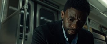 Movie still from “21 Bridges” (2019), directed by Brian Kirk – A man sitting on a train looking down at his face; Close Up shot, Over the shoulder angle