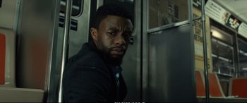 Movie still from “21 Bridges” (2019), directed by Brian Kirk – A man in a black jacket standing in front of a train; Close Up shot, Low angle