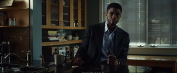 Movie still from “21 Bridges” (2019), directed by Brian Kirk – A man sitting at a table in a room; Medium shot, Low angle
