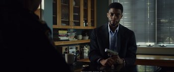 Movie still from “21 Bridges” (2019), directed by Brian Kirk – A man sitting at a table holding a cell phone; Medium shot, Over the shoulder angle