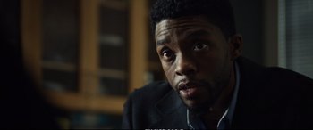 Movie still from “21 Bridges” (2019), directed by Brian Kirk – A person wearing a suit and tie; Close Up shot, Over the shoulder angle
