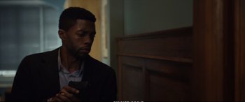 Movie still from “21 Bridges” (2019), directed by Brian Kirk – A man looking at his cell phone while sitting in a chair; Close Up shot, Over the shoulder angle