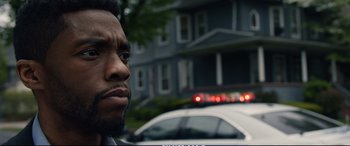 Movie still from “21 Bridges” (2019), directed by Brian Kirk – A man's face in front of a police car; Close Up shot, Low angle