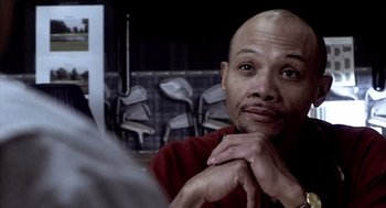 Movie still from “21 Grams” (2003), directed by Alejandro G. Iñárritu – A man with a bald head sitting in front of some chairs; Close Up shot, Over the shoulder angle