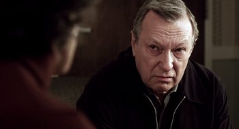 Movie still from “21 Grams” (2003), directed by Alejandro G. Iñárritu – An older man sitting on the floor with a cigarette in his mouth; Close Up shot, Over the shoulder angle