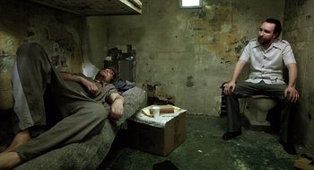 Movie still from “21 Grams” (2003), directed by Alejandro G. Iñárritu – Two men sitting on a couch in an abandoned room; Wide shot, High angle