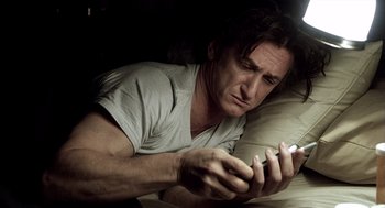 Movie still from “21 Grams” (2003), directed by Alejandro G. Iñárritu – A man sitting on a couch looking at a cell phone; Close Up shot, High angle