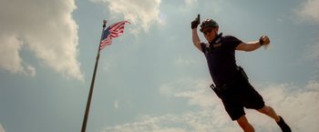 Movie still from “21 Jump Street” (2012), directed by Phil Lord – A police officer in a helmet is pointing to a flag; Medium shot, Low angle