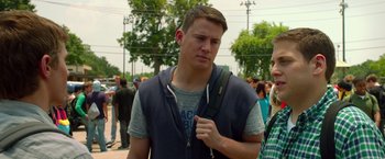 Movie still from “21 Jump Street” (2012), directed by Phil Lord – A young man is holding a backpack while standing in front of a group of onlookers; Close Up shot, Over the shoulder angle
