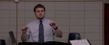 Movie still from “21 Jump Street” (2012), directed by Phil Lord – A man wearing a tie holding something in his hand; Medium shot, Over the shoulder angle