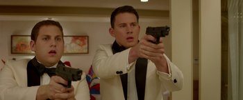 Movie still from “21 Jump Street” (2012), directed by Phil Lord – A man in a white suit holding a gun in front of a mirror; Medium shot, Over the shoulder angle