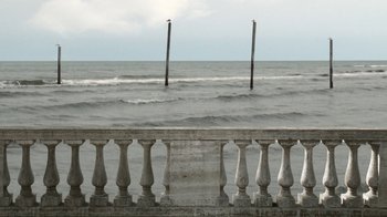 Movie still from “24 Frames” (2017), directed by Abbas Kiarostami – A view of the ocean from a balcony overlooking the water; Extreme Wide shot, Over the shoulder angle