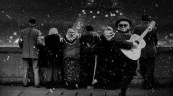 Movie still from “24 Frames” (2017), directed by Abbas Kiarostami – A black and white photo of a group of people standing in the snow; Wide shot, Low angle