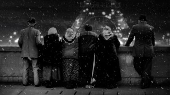 Movie still from “24 Frames” (2017), directed by Abbas Kiarostami – A black and white photo of people sitting on a bench in the snow; Wide shot, Low angle