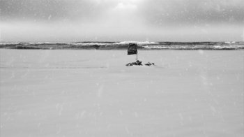 Movie still from “24 Frames” (2017), directed by Abbas Kiarostami – A black and white photo of a flag in the snow; Extreme Wide shot, High angle