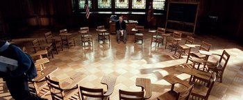 Movie still from “25th Hour” (2002), directed by Spike Lee – A man sitting on the floor in a circle of wooden chairs; Wide shot, High angle